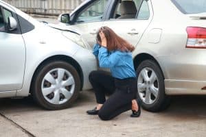 Distressed woman kneeling by two crashed cars, highlighting legal steps after a rental vehicle accident.